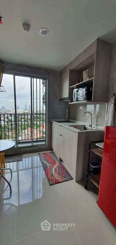 Modern kitchen with city view, featuring sleek cabinetry and vibrant red fridge.