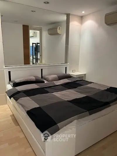 Modern bedroom with stylish decor and mirrored wall, featuring a comfortable bed and sleek air conditioning units.