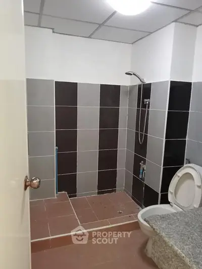 Modern bathroom with tiled shower area and toilet in a real estate property.