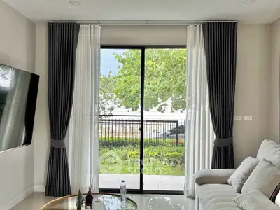 Modern living room with large window and garden view, featuring sleek furniture and elegant curtains.