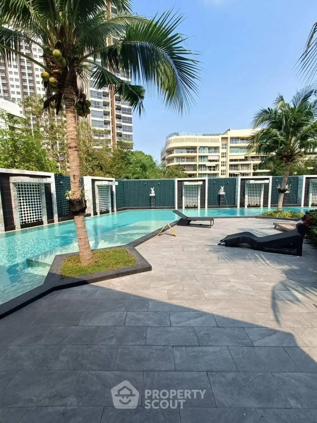Luxurious poolside area with palm trees and modern lounge chairs in a high-end residential complex.