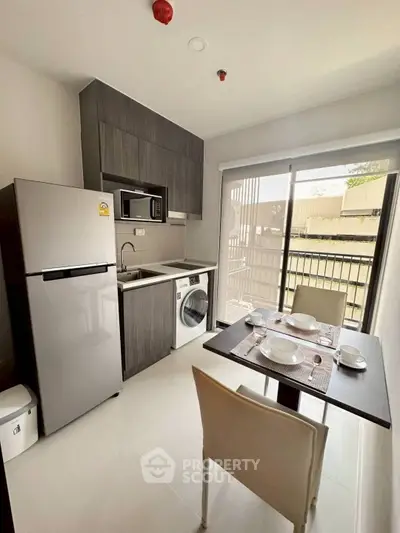 Modern compact kitchen with dining area, featuring fridge, microwave, and washing machine in a bright apartment.