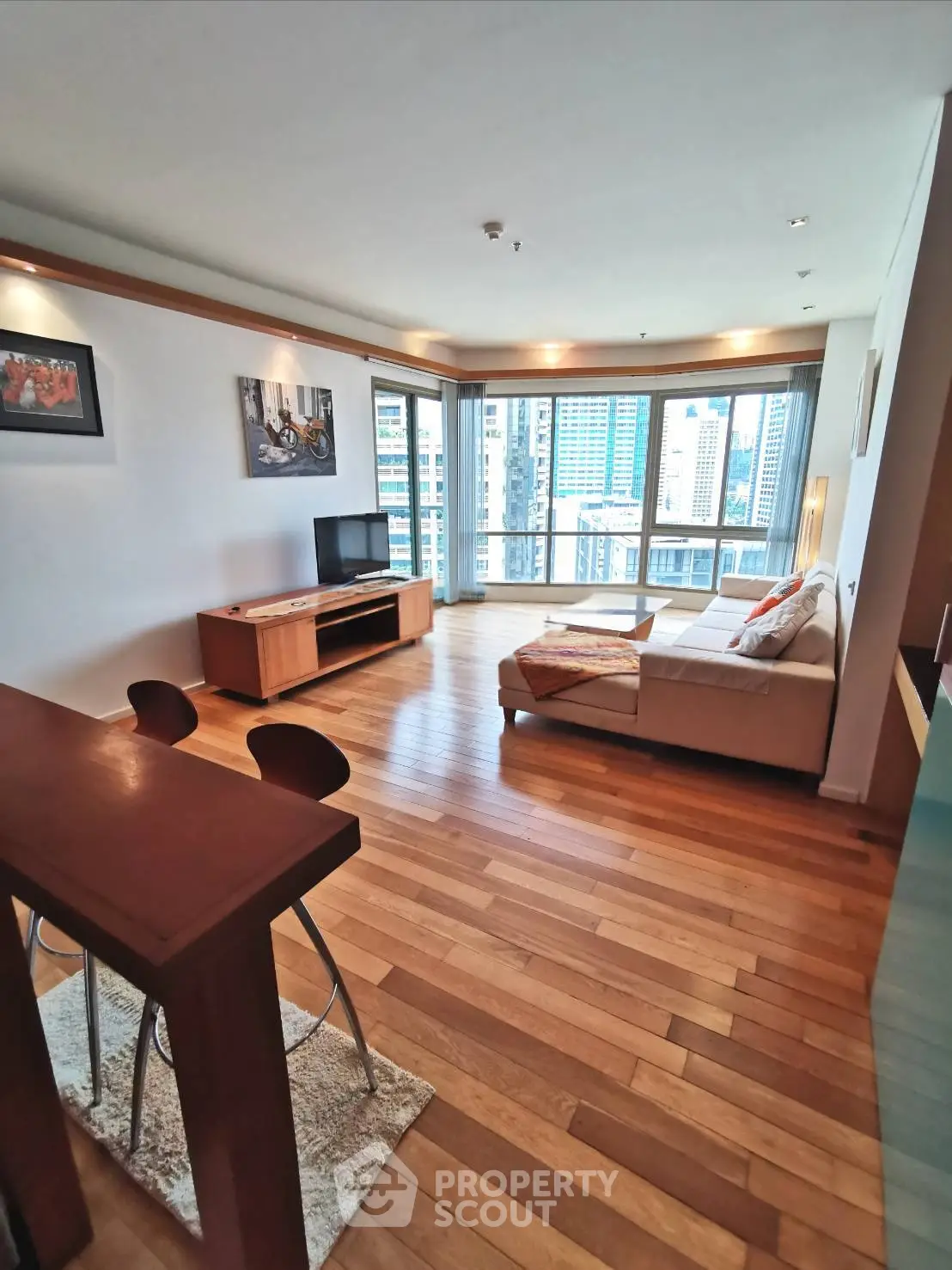Spacious living room with city view, modern decor, and wooden flooring in a high-rise apartment.