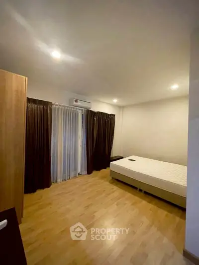 Spacious bedroom with wooden flooring and large window for natural light