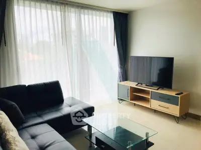 Modern living room with sleek black sofa, glass coffee table, and large TV, perfect for relaxation.