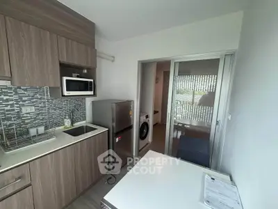 Modern kitchen with sleek cabinetry and appliances, featuring a microwave and fridge, adjacent to a laundry area.