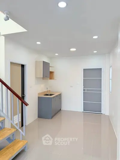 Modern minimalist kitchen with sleek cabinetry and staircase in a bright open space.