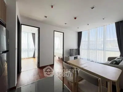 Modern apartment interior with open living and dining area, featuring large windows and natural light.