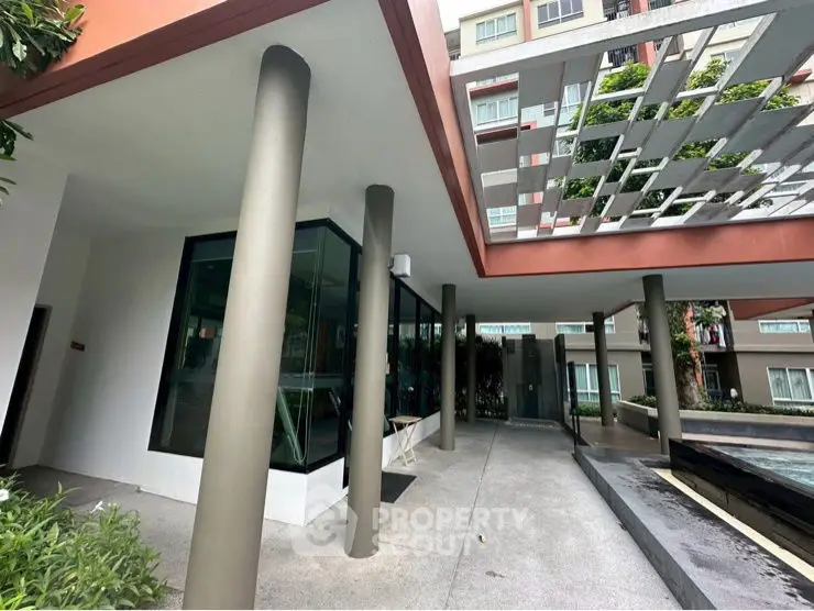 Modern apartment building entrance with stylish architectural design and greenery.