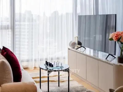 Modern living room with large TV, elegant decor, and city view through sheer curtains.