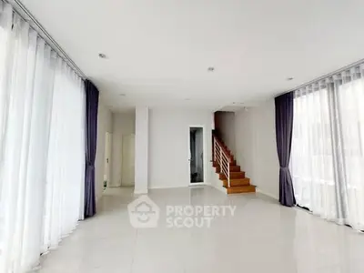 Spacious modern living room with elegant curtains and staircase, perfect for stylish living.