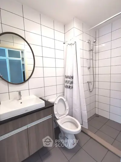 Modern bathroom with sleek tiles and round mirror, featuring a shower and vanity unit.