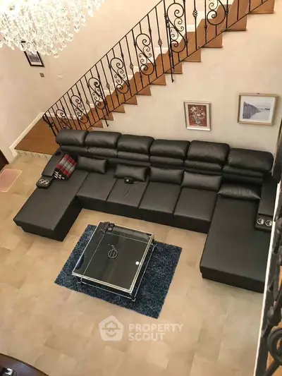 Luxurious living room with elegant staircase and modern black leather sectional sofa.