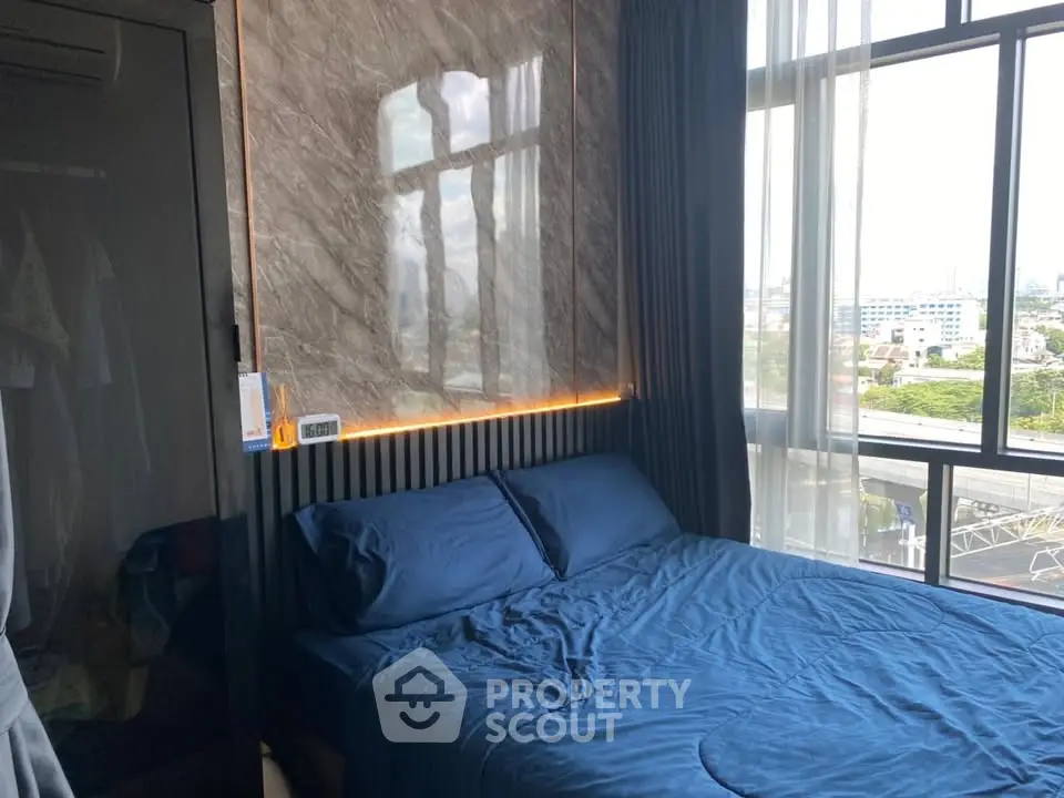 Modern bedroom with large window and city view, featuring stylish decor and cozy bedding.