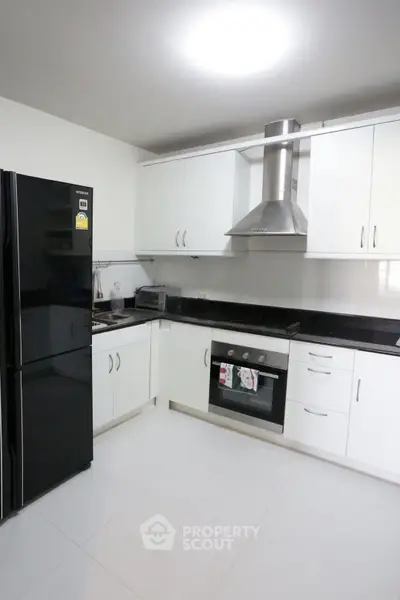 Modern kitchen with sleek black appliances and white cabinetry, featuring a built-in oven and stylish range hood.