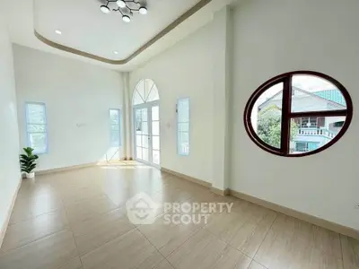 Spacious and bright room with unique circular window and modern lighting.