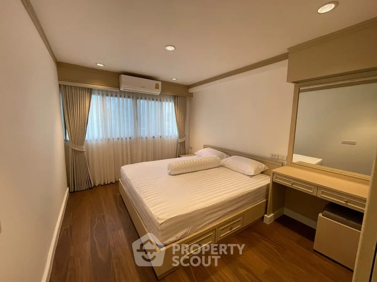 Spacious bedroom with elegant wooden flooring and ample natural light, featuring a cozy bed and stylish vanity.