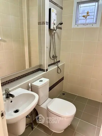 Modern bathroom with sleek fixtures and neutral tiles, featuring a shower and toilet.