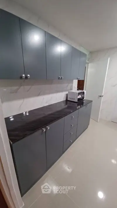 Modern kitchen with sleek cabinetry and marble backsplash, featuring a microwave and ample storage space.