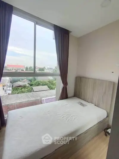 Cozy bedroom with large window offering scenic city view, perfect for relaxation and comfort.