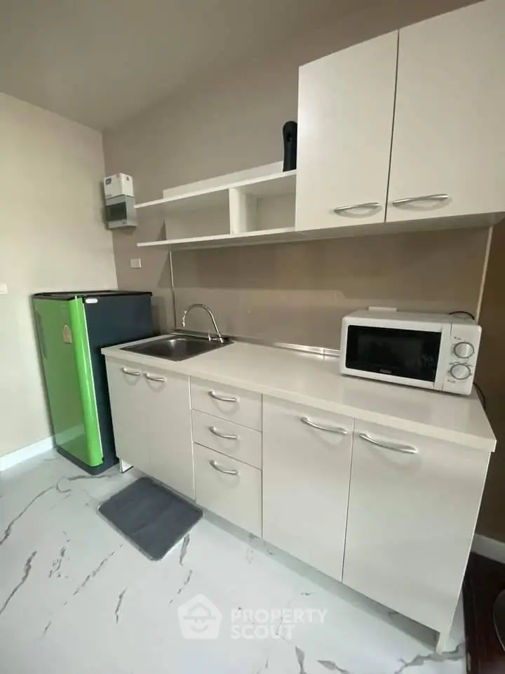 Modern kitchen with sleek cabinets, compact fridge, and microwave in a cozy apartment.