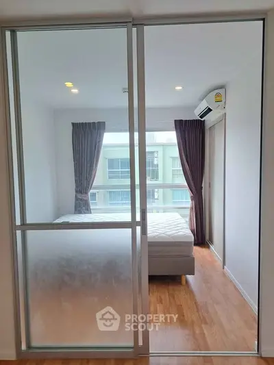 Modern bedroom with sliding glass door and natural light, featuring wooden flooring and air conditioning.