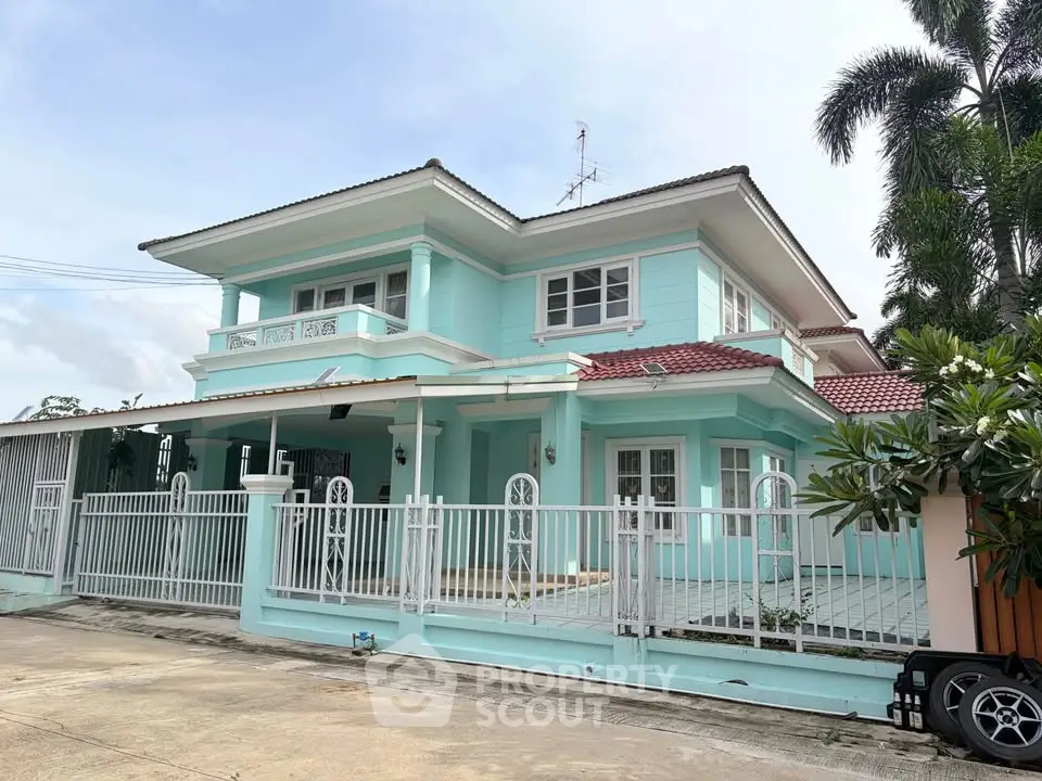 Charming two-story turquoise house with a spacious driveway and lush greenery, perfect for family living.