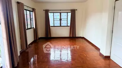 Spacious empty room with polished wooden floors and large windows, perfect for customization.