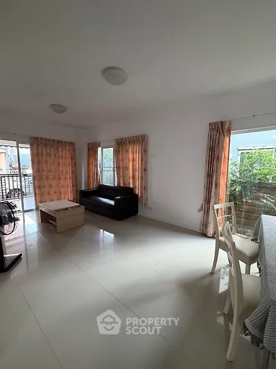 Spacious living room with large windows and balcony access, featuring modern furniture and natural light.
