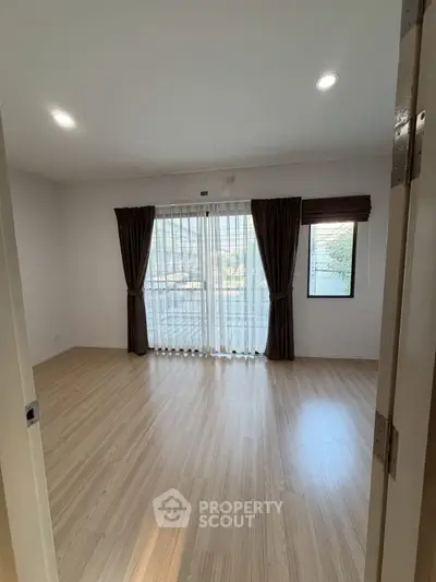 Spacious empty room with wooden flooring and large windows, perfect for customization.