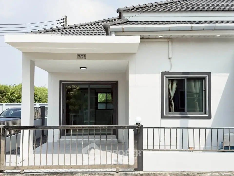 Modern single-story house with sleek design and gated entrance, featuring a tiled roof and large windows.