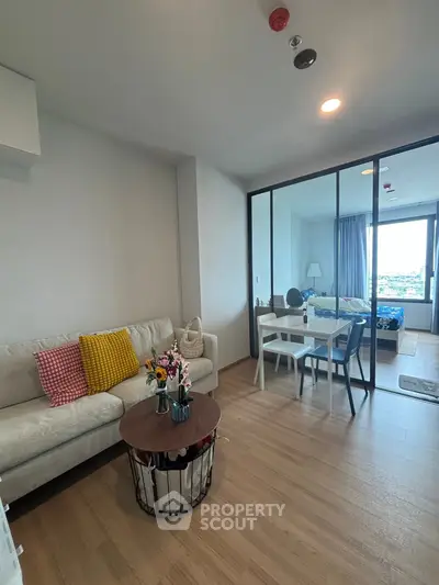 Modern living room with cozy seating and glass partition to bedroom, bright and inviting space.