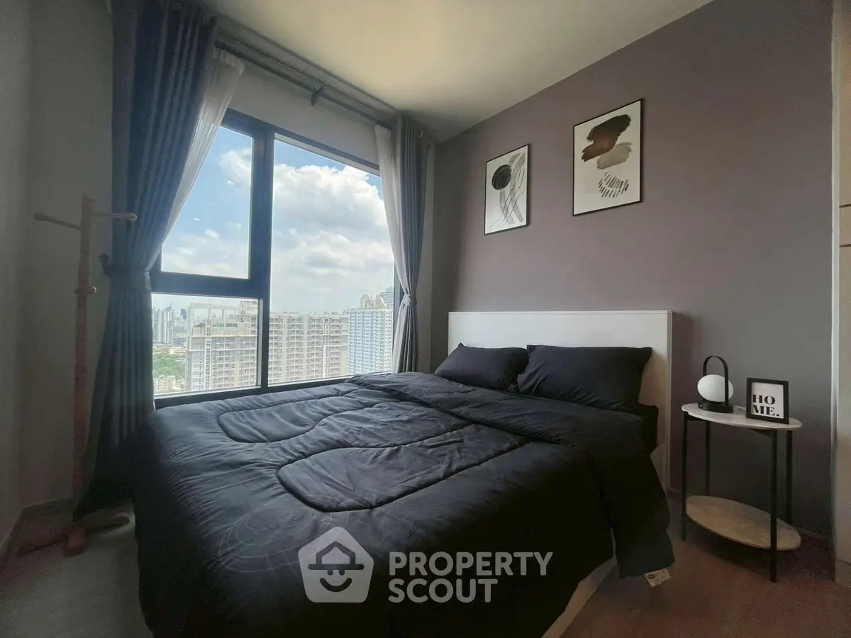 Modern bedroom with large window offering stunning city views, stylish decor, and cozy ambiance.