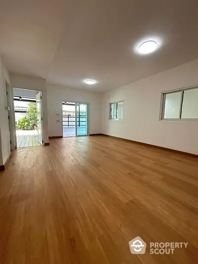 Spacious empty room with wooden flooring and large windows for natural light.