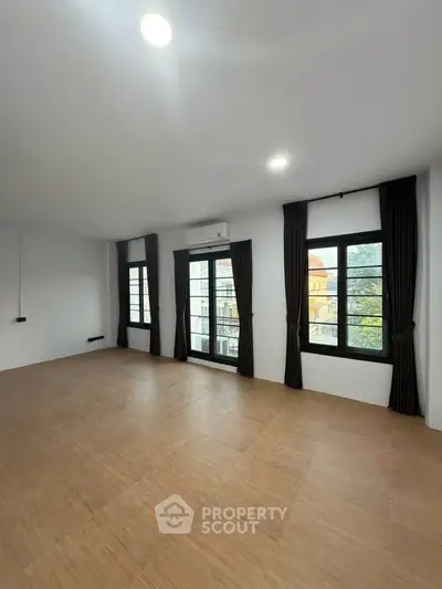 Spacious empty room with large windows and wooden flooring, ideal for customization.