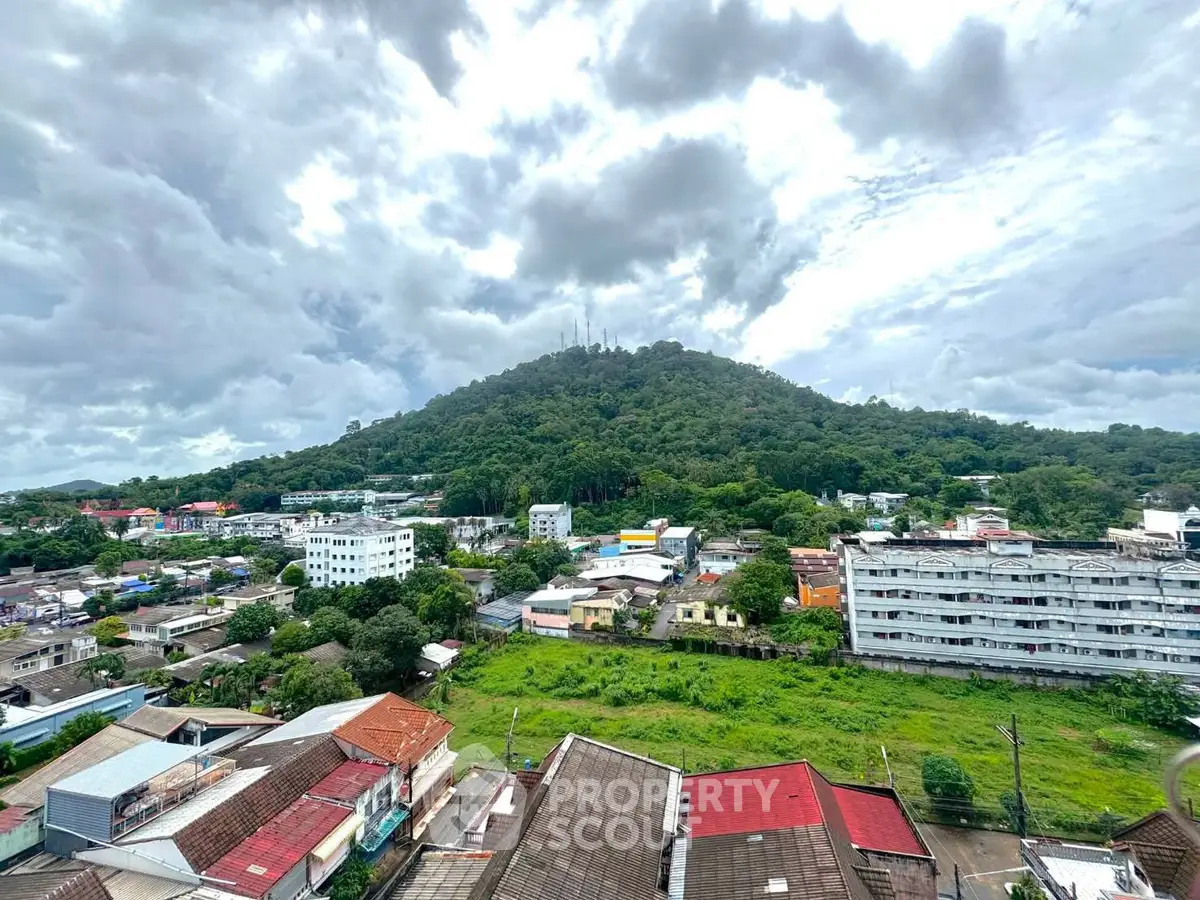 Scenic view of urban landscape with lush green hill under cloudy sky, perfect for real estate investment.