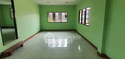 Spacious empty room with green walls and large windows offering natural light.