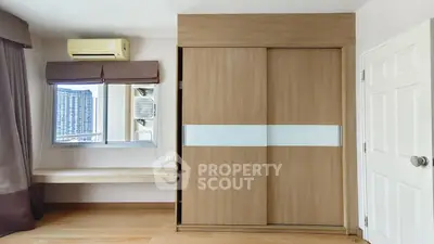 Modern bedroom with built-in wardrobe and city view window, featuring sleek wooden finishes and air conditioning.
