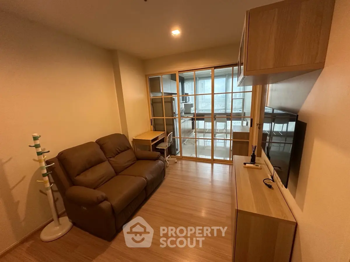 Cozy living room with brown leather sofa and wooden furniture, featuring a sliding glass door to the kitchen.