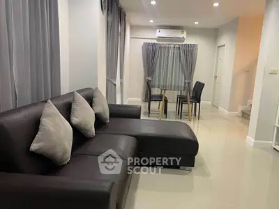 Modern living room with sleek black sofa and dining area, featuring elegant gray curtains and bright lighting.
