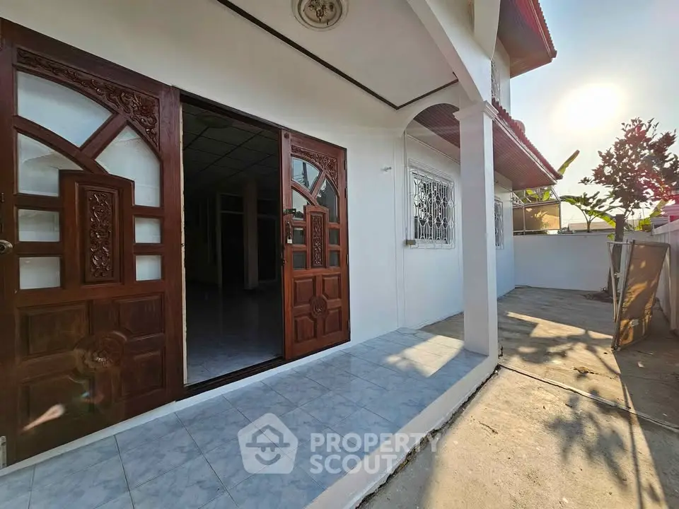 Charming home entrance with elegant wooden doors and spacious outdoor area, perfect for relaxation.