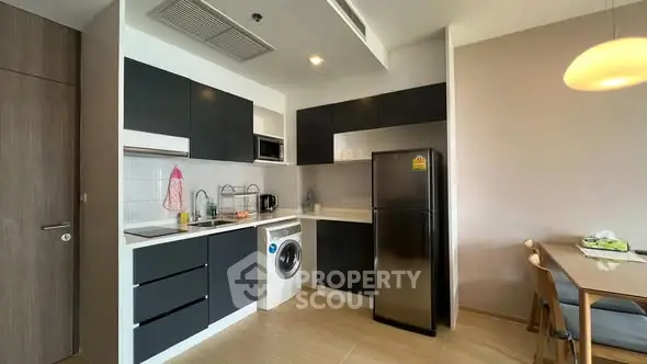 Modern kitchen with sleek black cabinets, washing machine, and dining area in stylish apartment.