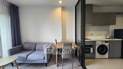 Modern living room with open kitchen and washing machine, featuring a cozy sofa and dining area.
