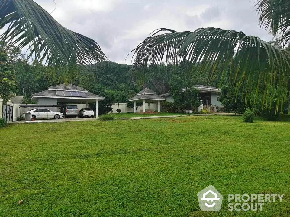 Lush tropical oasis with spacious lawn and twin single-story homes featuring covered parking and serene mountain backdrop.