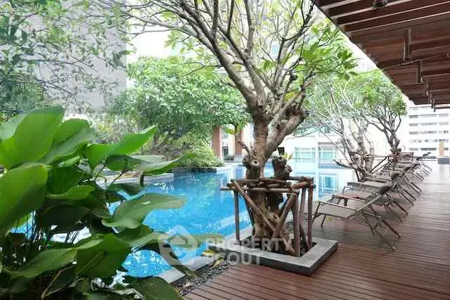 Luxurious poolside area with lush greenery and modern lounge chairs.