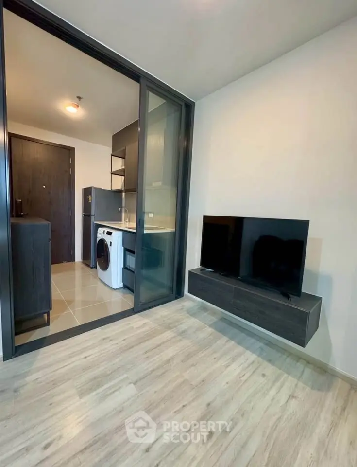 Modern apartment with sleek kitchen and living area featuring a washing machine and mounted TV.