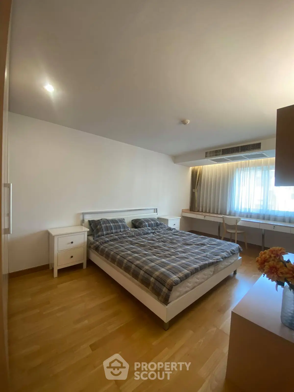 Spacious bedroom with wooden flooring and natural light, featuring a cozy bed and modern furniture.