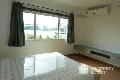 Bright bedroom with large window offering stunning river view and air conditioning.