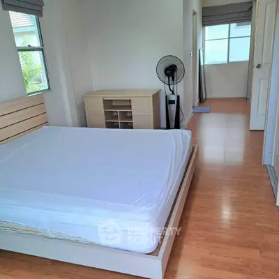Spacious bedroom with wooden flooring and natural light, featuring a modern bed and storage unit.