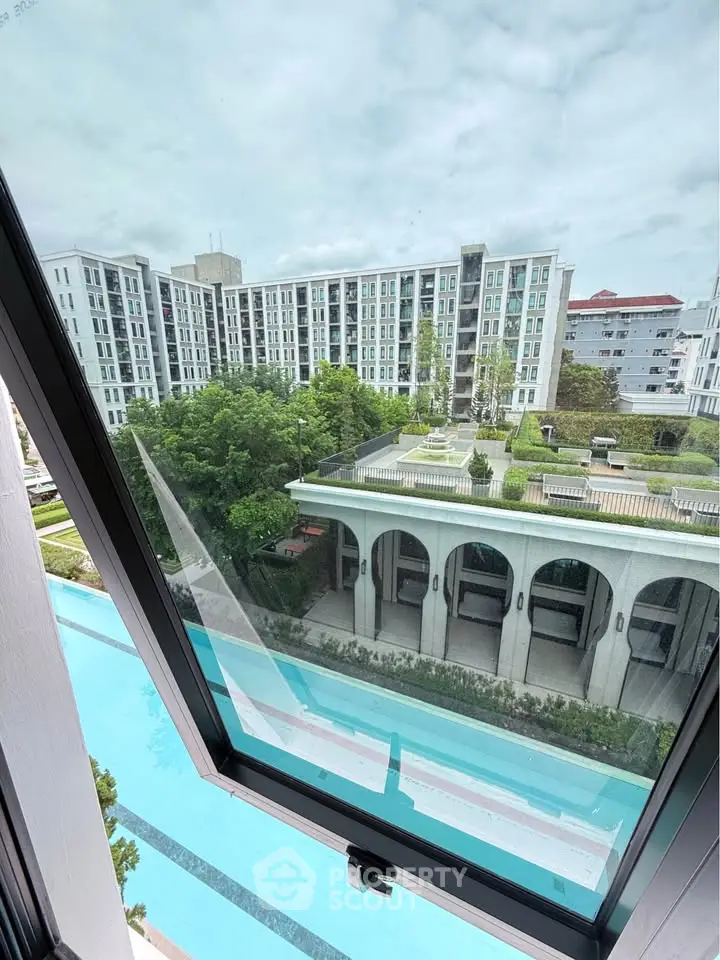 Stunning view from window overlooking modern apartment complex with pool and lush greenery.
